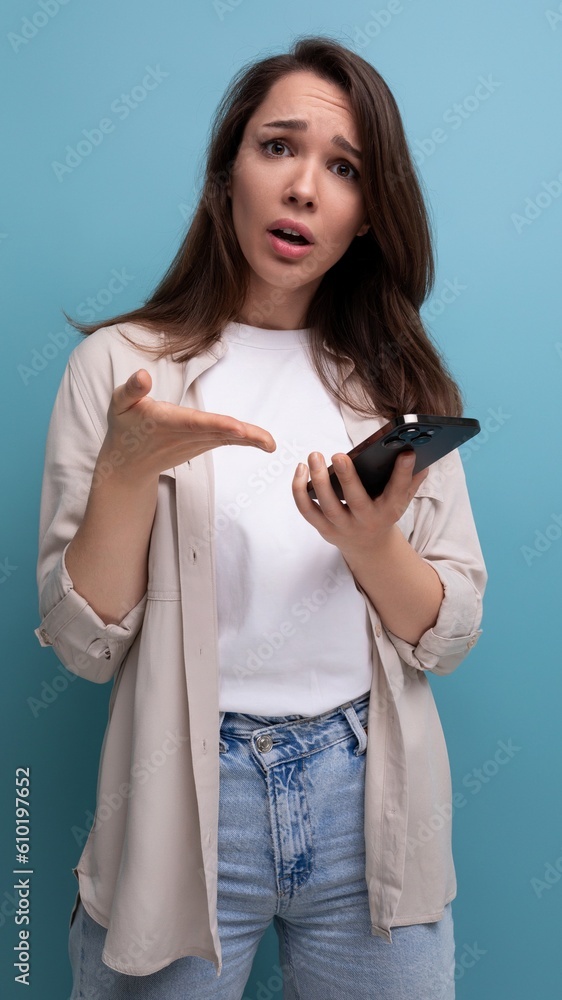 upset cute brunette young brunette lady dressed in a shirt and jeans holding a phone in her hands upset cute brunette young brunette lady dressed in a shirt and jeans holding a phone in her hands