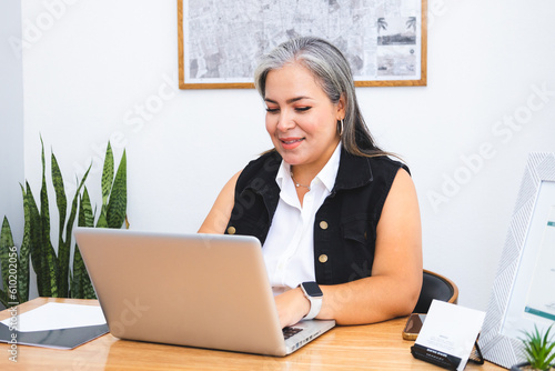 Latin executive woman with gray hair working with laptop