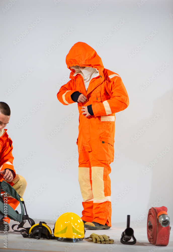 Firefighter is standing zipping up his uniform while a professional firefighter prepares equipment for his partner to wear on white background, Teamwork for work. Firefighter is standing zipping up his uniform while a professional firefighter prepares equipment for his partner to wear on white background, Teamwork for work.