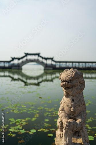 Chinese traditional style stone lion with wooden bridge and lotus pool in background © imphilip