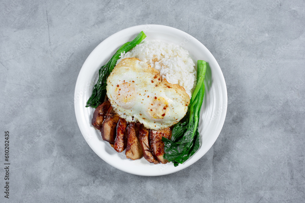 A top down view of a plate of BBQ pork, fried eggs and steamed white rice.