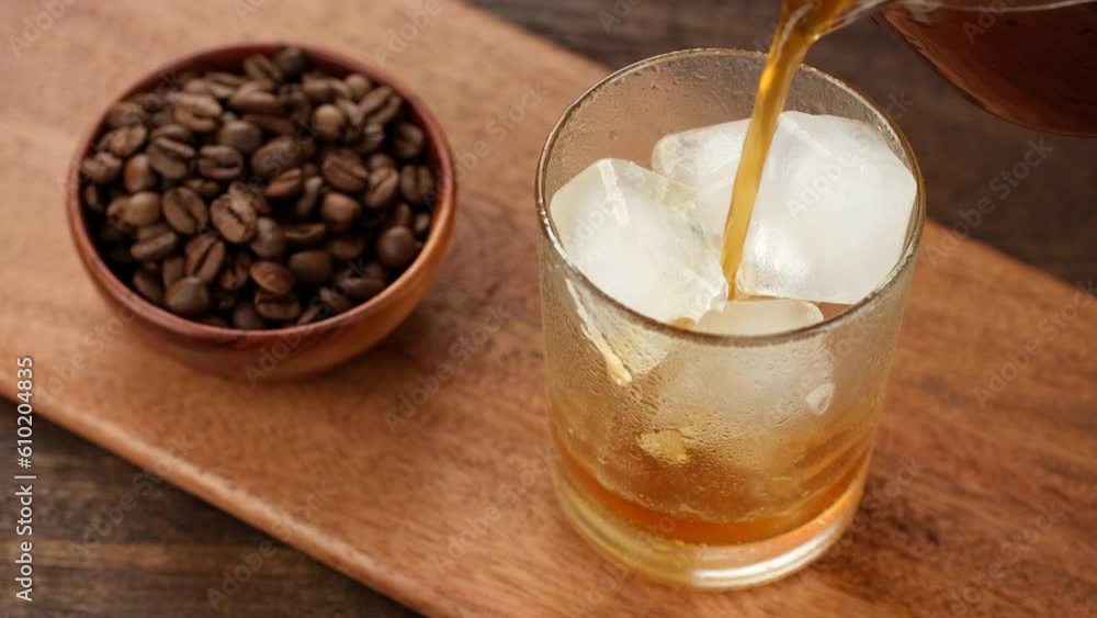 Pouring black coffee in glass with ice. Making iced coffee