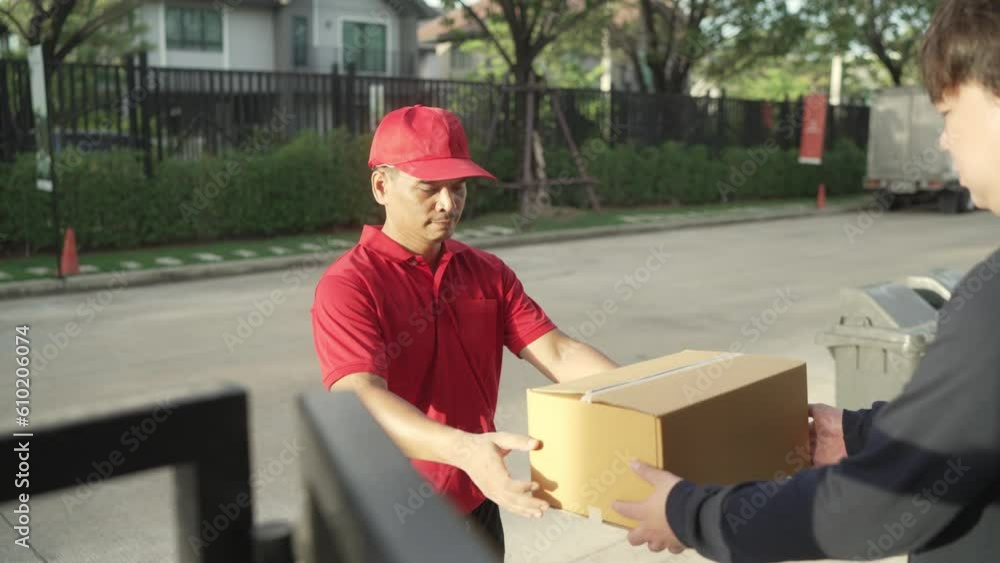 A parcel delivery worker wearing a red uniform is holding a parcel box to the recipient. contact the receiver in front of the house
