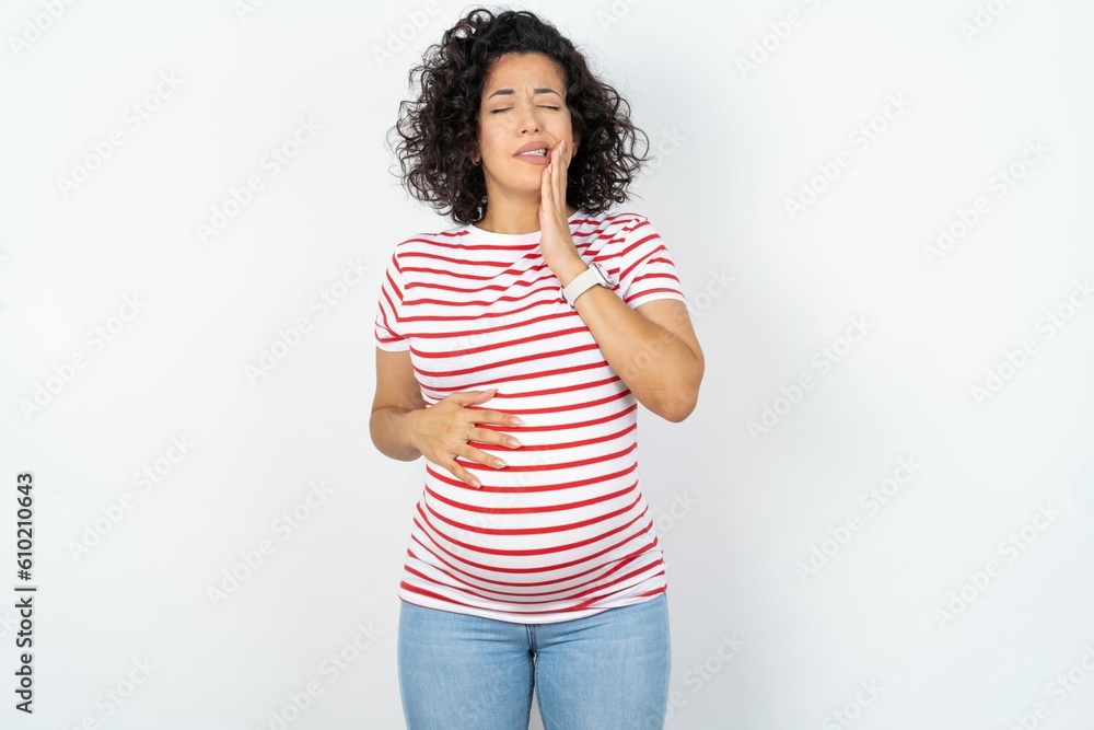 young pregnant woman wearing striped t-shirt over white background touching mouth with hand with painful expression because of toothache or dental illness on teeth. young pregnant woman wearing striped t-shirt over white background touching mouth with hand with painful expression because of toothache or dental illness on teeth.