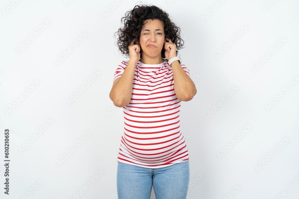 young pregnant woman wearing striped t-shirt over white background covering ears with fingers with annoyed expression for the noise of loud music. Deaf concept. young pregnant woman wearing striped t-shirt over white background covering ears with fingers with annoyed expression for the noise of loud music. Deaf concept.