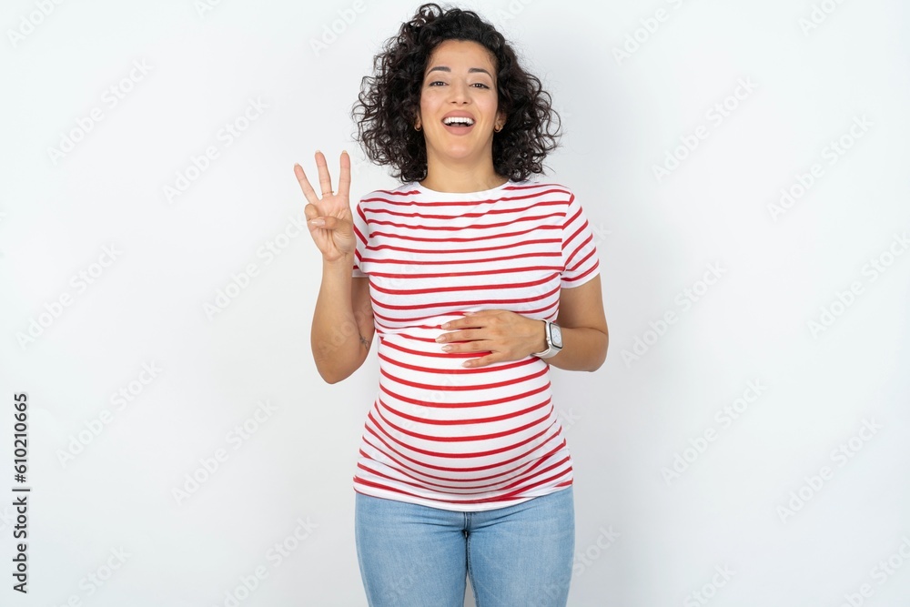 young pregnant woman wearing striped t-shirt over white background showing and pointing up with fingers number three while smiling confident and happy. young pregnant woman wearing striped t-shirt over white background showing and pointing up with fingers number three while smiling confident and happy.