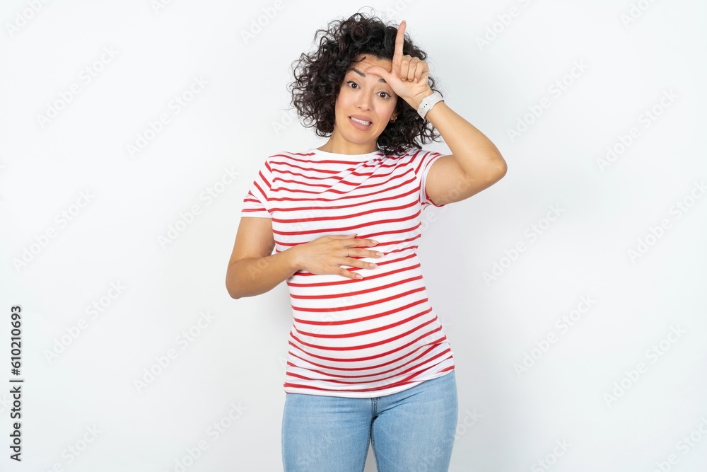 Φωτογραφία young pregnant woman wearing striped t-shirt over white background making fun of people with fingers on forehead doing loser gesture mocking and insulting