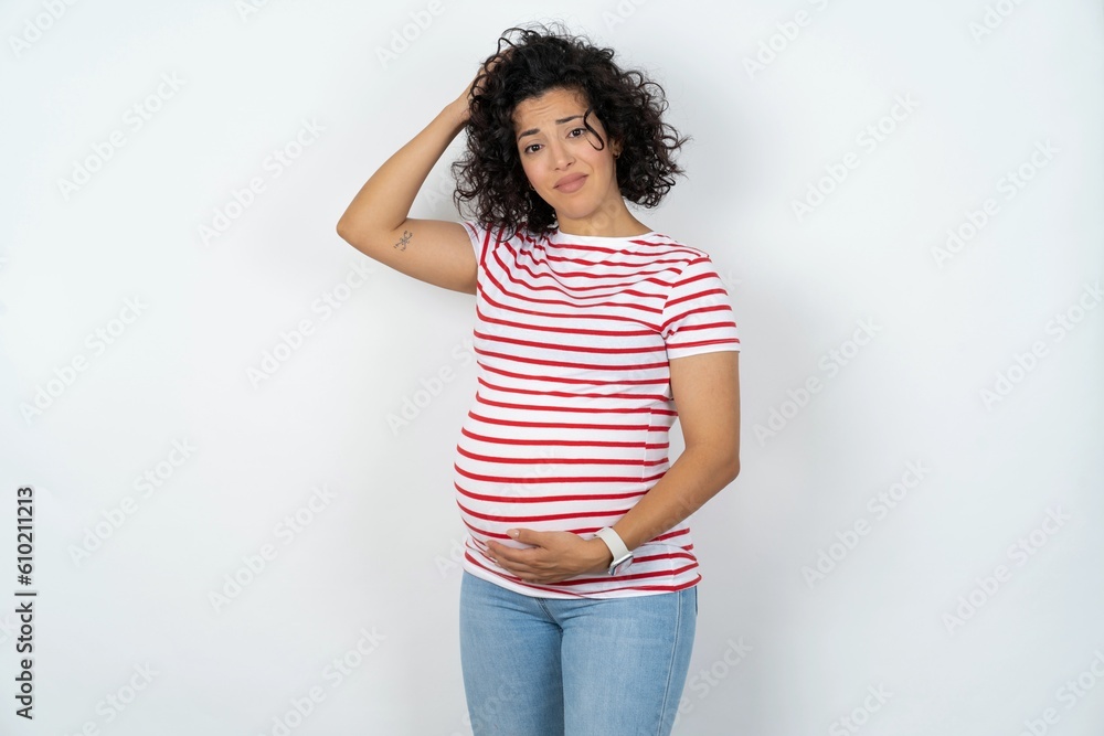 young pregnant woman wearing striped t-shirt over white background being confused and wonders about something. Holding hand on head, uncertain with doubt. Pensive concept. - obrazy, fototapety, plakaty 