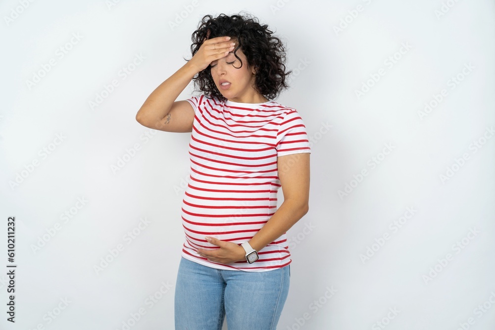 young pregnant woman wearing striped t-shirt over white background Touching forehead for illness and fever, flu and cold, virus sick. young pregnant woman wearing striped t-shirt over white background Touching forehead for illness and fever, flu and cold, virus sick.