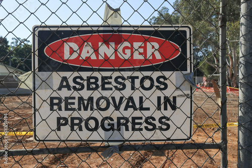 black, white and red Danger Asbestos Removal In Progress warning site on wire fence