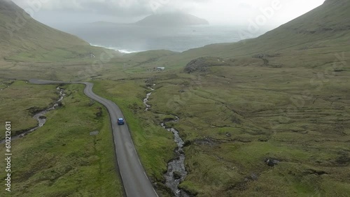 Fantastic aerial tracking shot of a blue car heading downhill and on the famous winding road that leads to Norðradalur in the Faroe Islands. photo