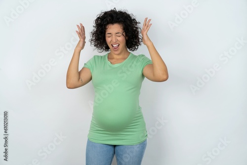 young pregnant woman wearing green t-shirt over white background goes crazy as head goes around feels stressed because of horrible situation