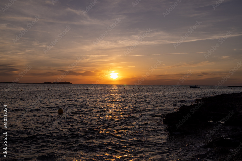 Photo of the beach at sunset on the town of Sant Antoni de Portmany on the island of Ibiza in the Balearic Islands Spain with the ocean waves and the sun reflecting on the water