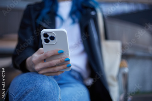 Young woman browsing a mobile app on a modern smart phone with triple camera. Unrecognizable female person sitting on a bench and using a cell phone