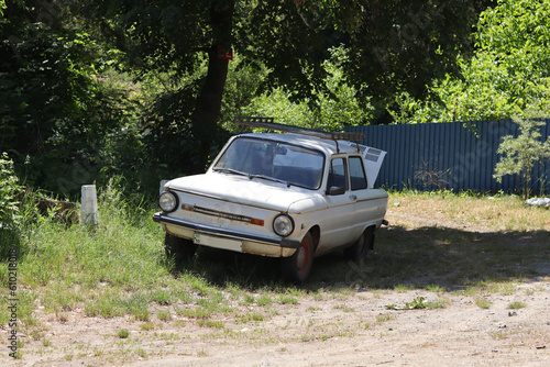Canvas Print A white retro subcompact car, Soviet-made in the 1970s, parked on the side of a sandy road near a lake