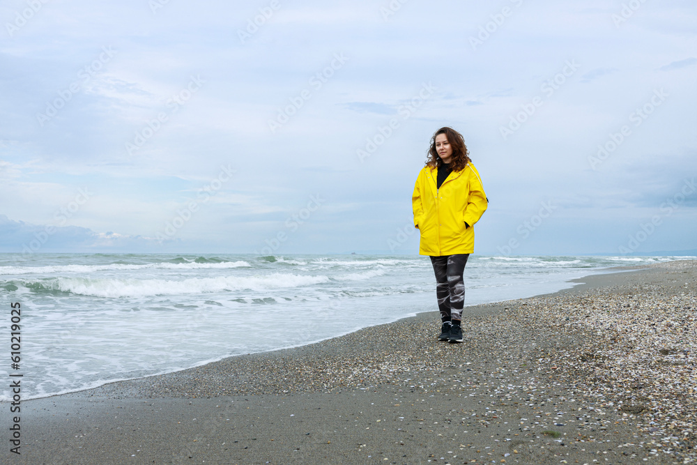 Woman wearing yellow raincoat walking on the beach on a rainy day
