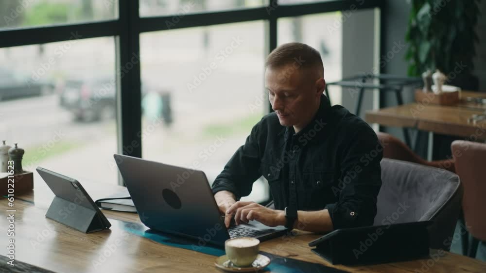 Remote Work In Cafe In Big City, Adult Man Freelancer Or Trader Typing Messages On Laptop Keyboard Remote Work In Cafe In Big City, Adult Man Freelancer Or Trader Typing Messages On Laptop Keyboard