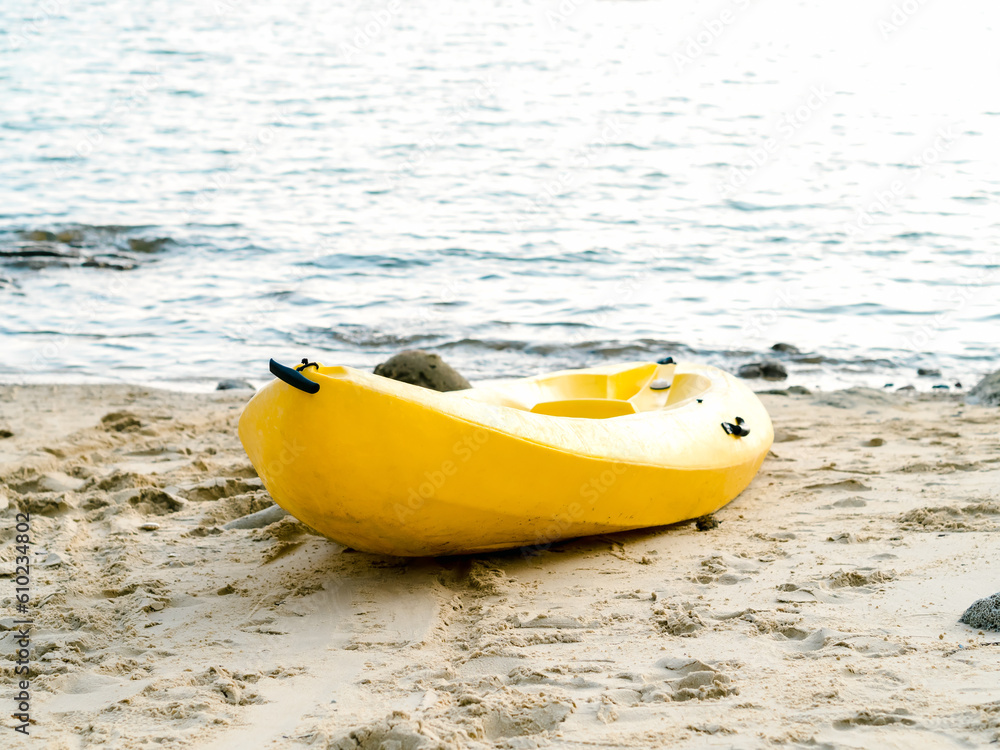 Obraz premium A yellow kayak boat on sandy beach and blue sea background with nobody, activity equipment prepare for hotel or resort guests on holiday summer vacation travel.