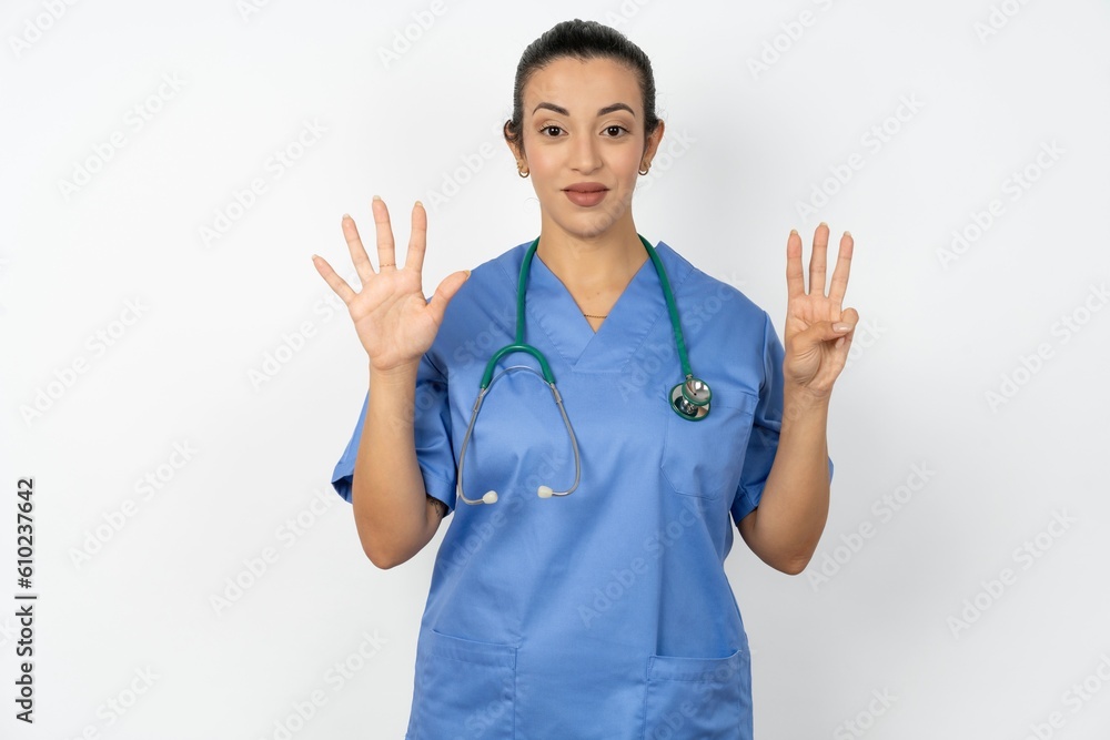 Young doctor woman wearing blue uniform over isolated background showing and pointing up with fingers number eight while smiling confident and happy.