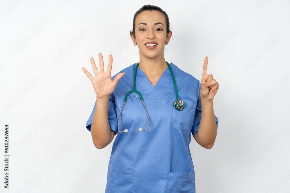 Young doctor woman wearing blue uniform over isolated background showing and pointing up with fingers number six while smiling confident and happy. Young doctor woman wearing blue uniform over isolated background showing and pointing up with fingers number six while smiling confident and happy.