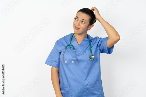 Young doctor woman wearing blue uniform over isolated background being confused and wonders about something. Holding hand on head, uncertain with doubt. Pensive concept.