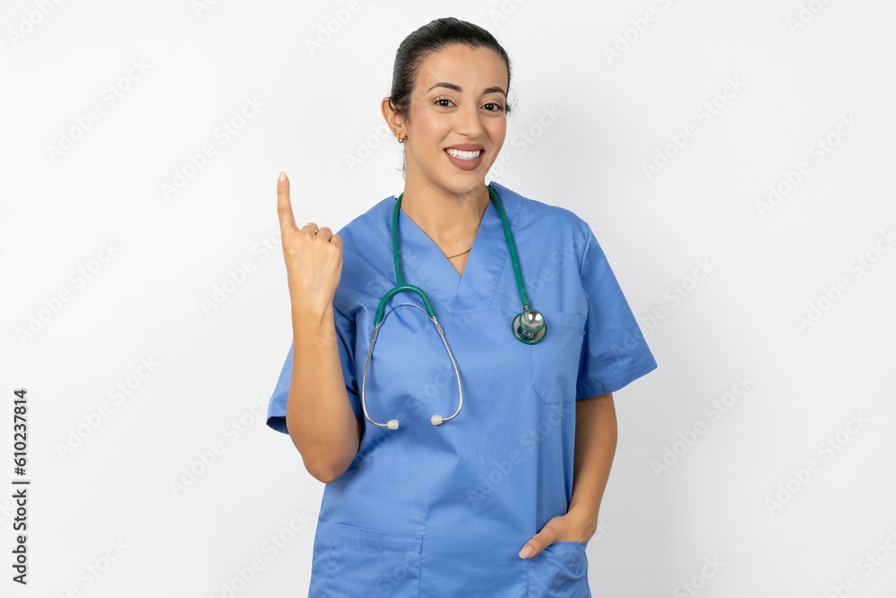 Young doctor woman wearing blue uniform over isolated background smiling and looking friendly, showing number one or first with hand forward, counting down Young doctor woman wearing blue uniform over isolated background smiling and looking friendly, showing number one or first with hand forward, counting down