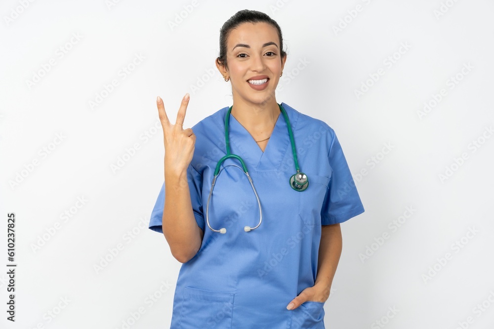Young doctor woman wearing blue uniform over isolated background smiling and looking friendly, showing number two or second with hand forward, counting down Young doctor woman wearing blue uniform over isolated background smiling and looking friendly, showing number two or second with hand forward, counting down