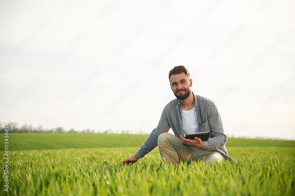 Sitting, holding notepad and checking quality of wheat. Handsome young man is on agricultural field Sitting, holding notepad and checking quality of wheat. Handsome young man is on agricultural field