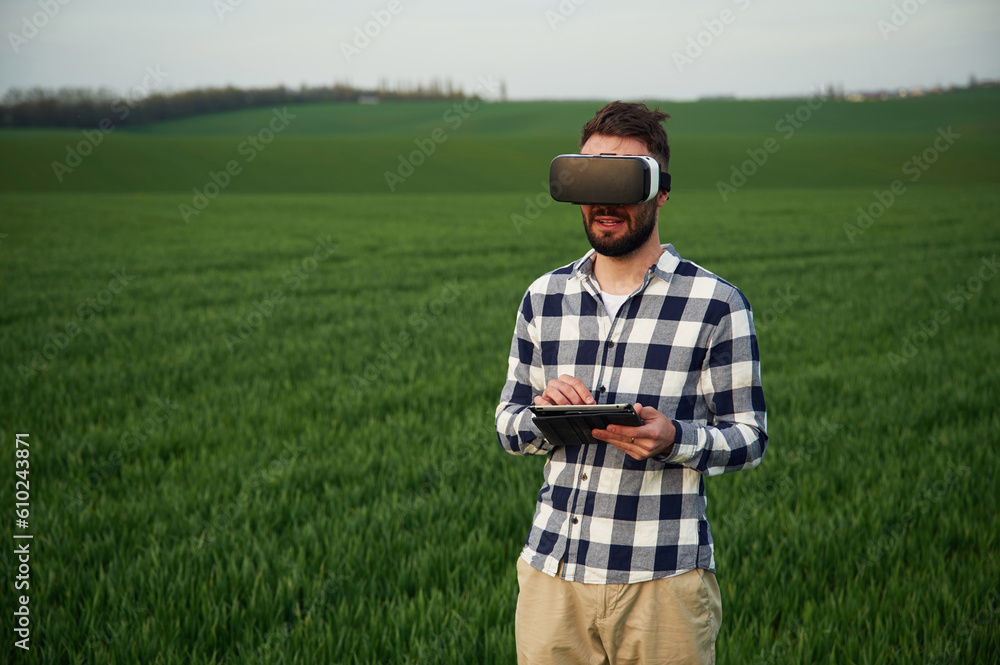 In virtual reality glasses. Handsome young man is on agricultural field - obrazy, fototapety, plakaty 