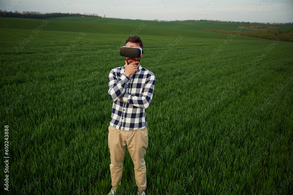 Playing game in VR glasses. Handsome young man is on agricultural field - obrazy, fototapety, plakaty 