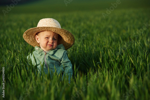 In cute straw hat. Little baby boy is in the agricultural field at daytime