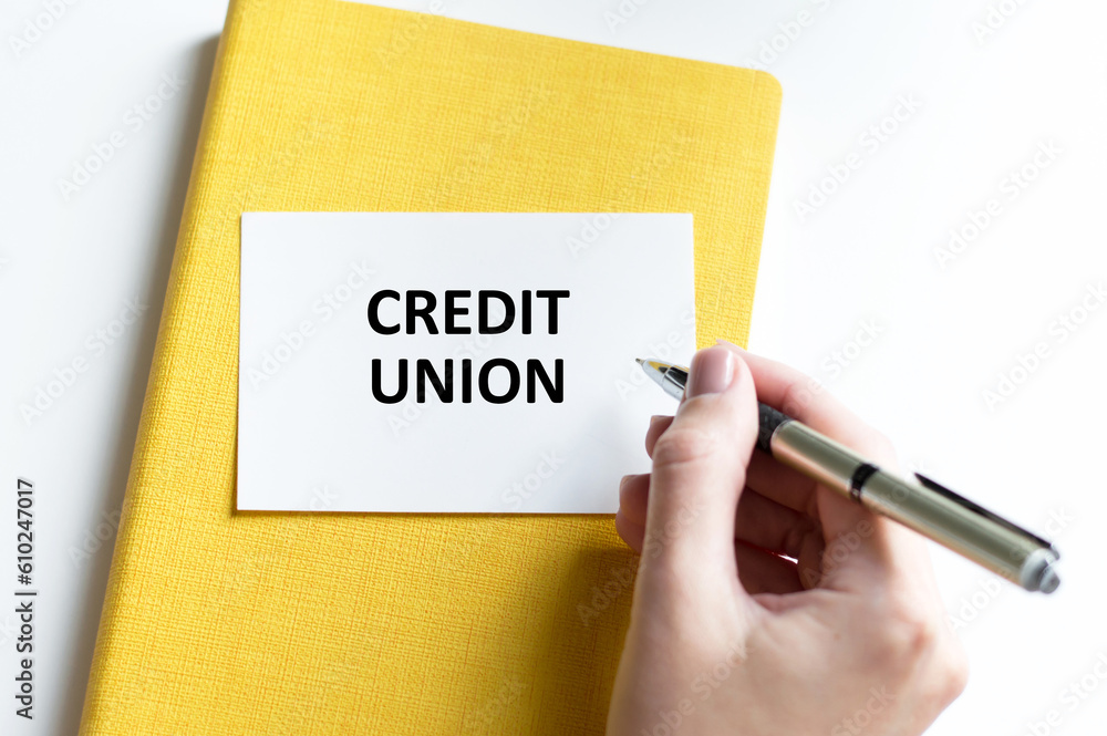 Credit Union text on a white card on a yellow notebook next to a man's hand with a pen Credit Union text on a white card on a yellow notebook next to a man's hand with a pen
