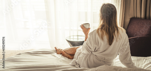 Woman in white bathrobe lying on sofa and relaxing with cup of tea at home.