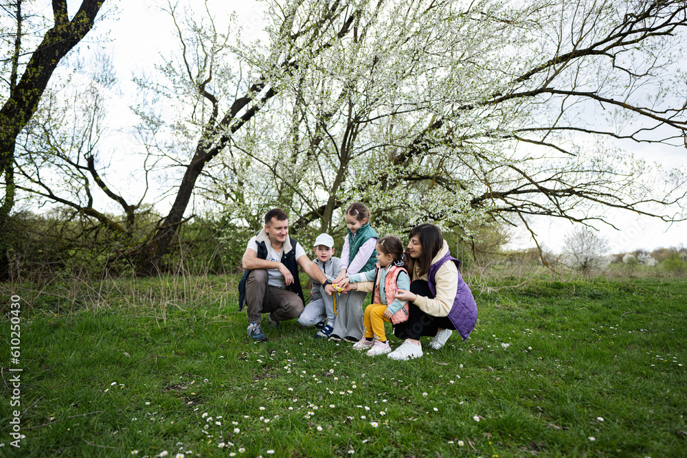 Family with three kids in spring meadow on the background of a flowering tree.