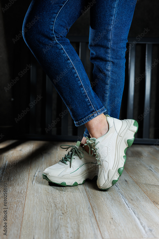 White leather summer sneakers on female legs in jeans. Women's casual sneakers. Comfortable women's shoes