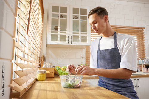 Fotografiet young man preparing vegetable salad in the kitchen