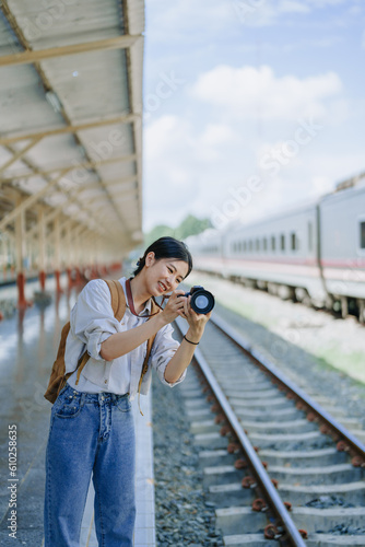 Asian teenage girl traveling using a camera take a photo to capture memories while waiting for a train at the station. © Jirapong