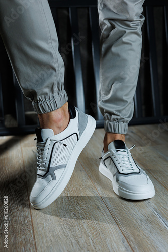 Male legs in white leather summer shoes. Comfortable men's white sneakers with laces. Casual men's sneakers