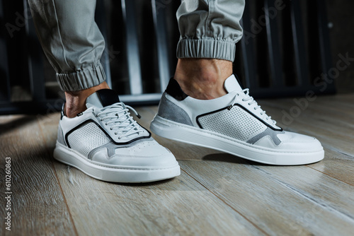 Male legs in white leather summer shoes. Comfortable men's white sneakers with laces. Casual men's sneakers