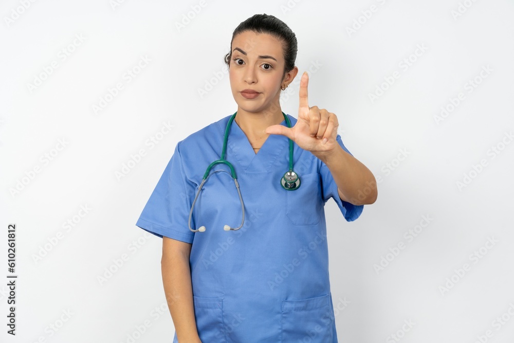 Beautiful doctor woman standing over white studio background making fun of people with fingers on forehead doing loser gesture mocking and insulting. Beautiful doctor woman standing over white studio background making fun of people with fingers on forehead doing loser gesture mocking and insulting.