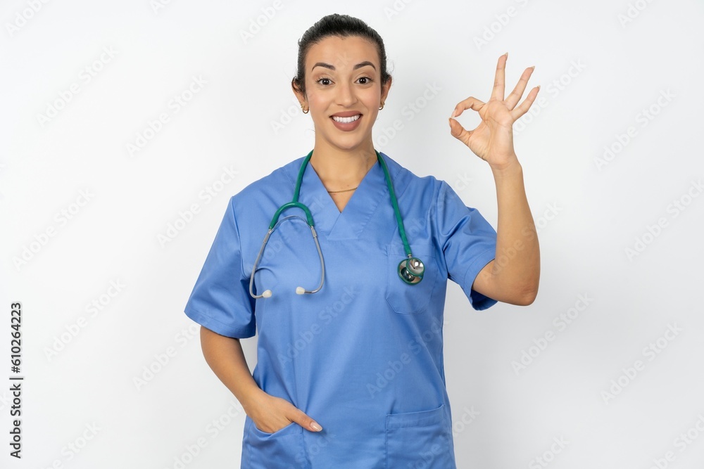 Beautiful doctor woman standing over white studio background hold hand arm okey symbol toothy approve advising novelty news