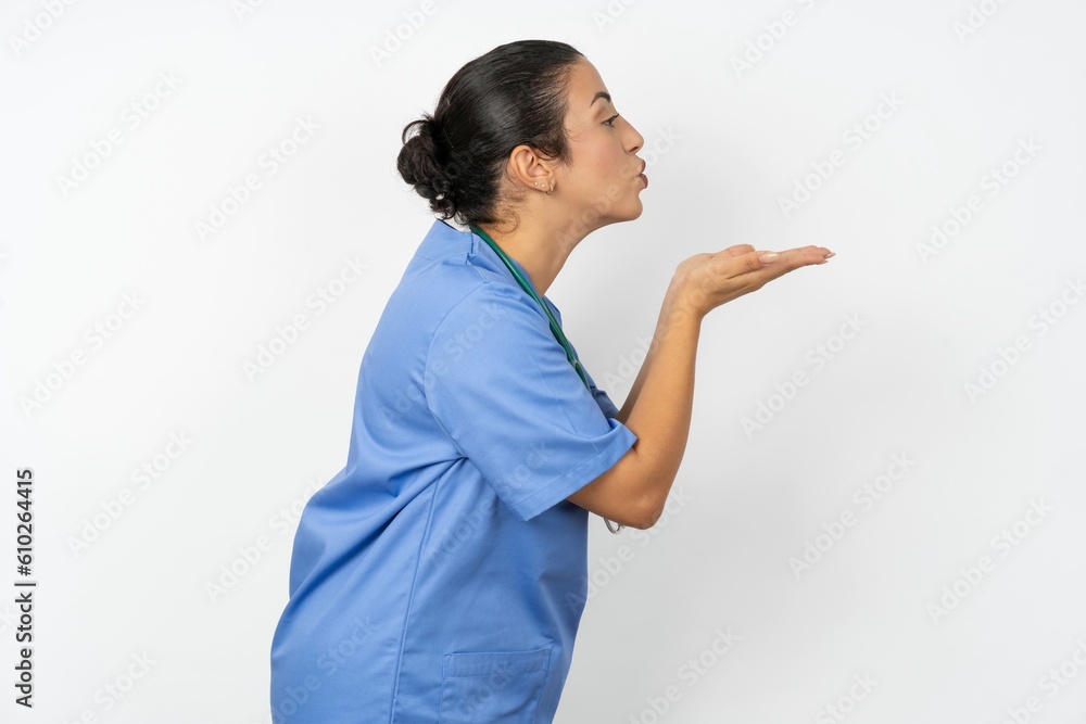 Profile side view, portrait of attractive Beautiful doctor woman standing over white studio background sending air kiss Profile side view, portrait of attractive Beautiful doctor woman standing over white studio background sending air kiss