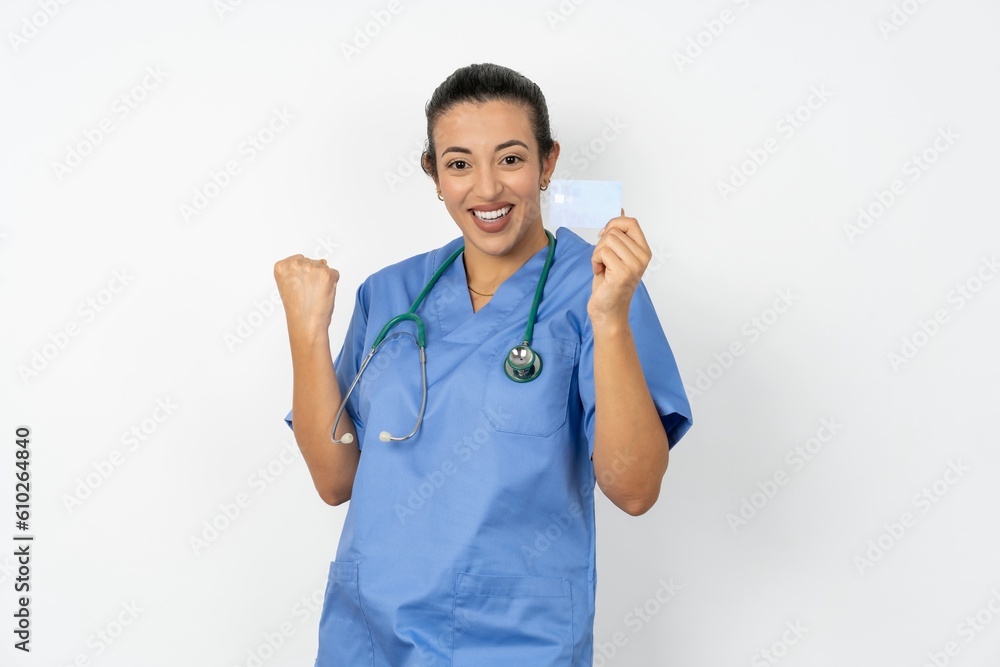 Excited happy positive cheerful smiling Beautiful doctor woman standing over white studio background hold credit card raise fist in victory Excited happy positive cheerful smiling Beautiful doctor woman standing over white studio background hold credit card raise fist in victory