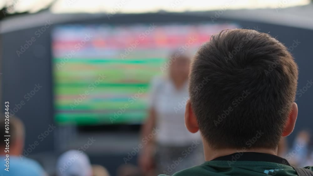 Little boy fan watching football match in fan zone, rear view Little boy fan watching football match in fan zone, rear view