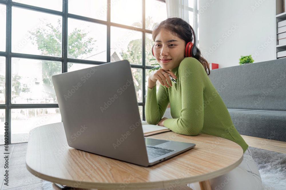 Naklejka premium Beautiful young asian woman choose music from laptop take a rest and listening song with headphone. Lifestyle in living room at house in the morning. Relaxing time in living room
