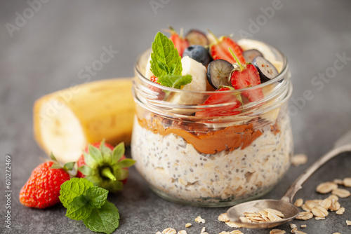 Healthy diet breakfast. Overnight oatmeal with chia seeds, bananas, strawberry and blueberry in a glass jar on a gray concrete background. photo