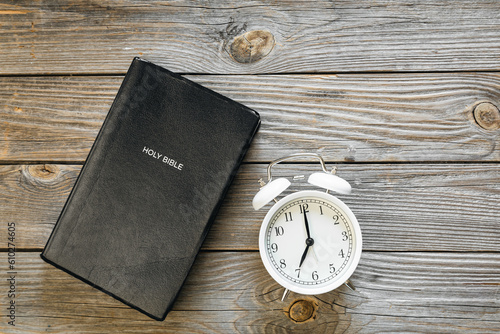 Bible book and white alarm clock on wooden background, concept of christianity and religion, copy space.