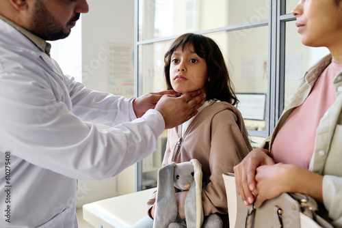 Pediatrician examining the sore throat of little girl while she visiting doctor with mom photo