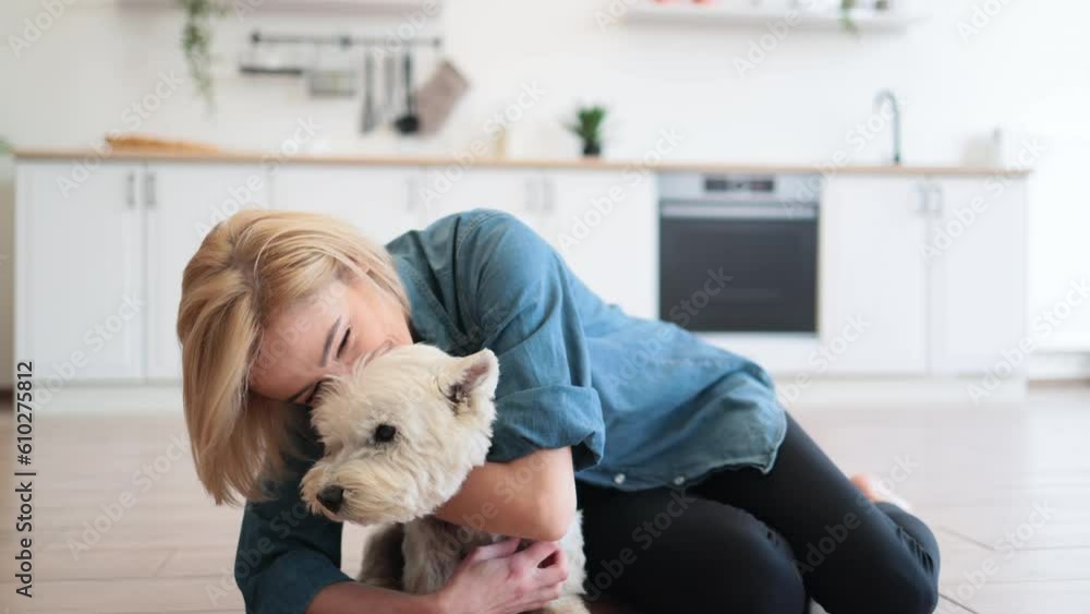 Portrait of smiling woman hugging gently adorable dog while posing on wooden floor with legs crossed. Happy female owner showing care for beloved pet before going for after dinner walk to park. Portrait of smiling woman hugging gently adorable dog while posing on wooden floor with legs crossed. Happy female owner showing care for beloved pet before going for after dinner walk to park.