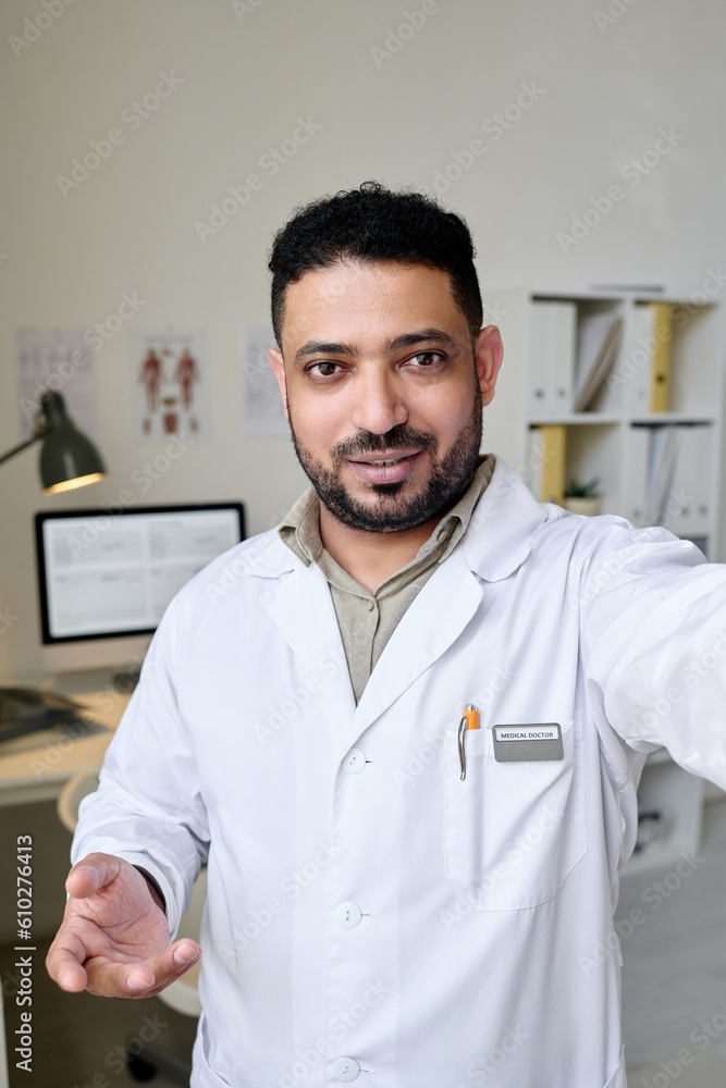 Vertical image of doctor in white coat looking at camera during video call in office Vertical image of doctor in white coat looking at camera during video call in office